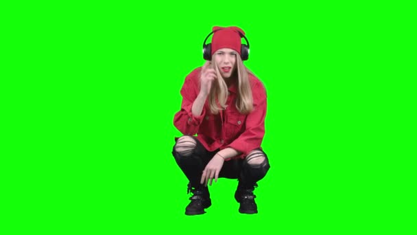 Girl sitting on her haunches and listening to music on headphones. Green screen — Stock Video