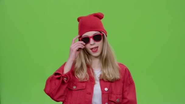Девушка в стильной одежде и красных очках флиртует и подмигивает. Зеленый экран — стоковое видео