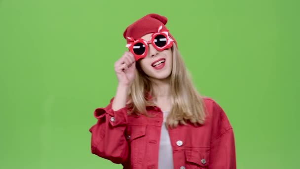 Adolescente en gafas divertidas construye muecas, guiños y muestra el idioma. Pantalla verde — Vídeos de Stock