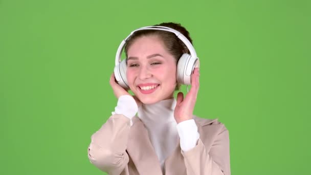 女性は、ヘッドフォンでメロディアスな曲を聴きます。緑色の画面。スローモーション — ストック動画