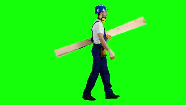 Οικοδόμος στο κράνος πηγαίνει να εργαστεί με ξύλινες σανίδες στα χέρια του. Πράσινη οθόνη. Πλάγια όψη — Αρχείο Βίντεο