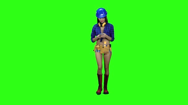 Chica en pantalones cortos y un casco está recogiendo sms en el teléfono contra un fondo verde — Vídeos de Stock