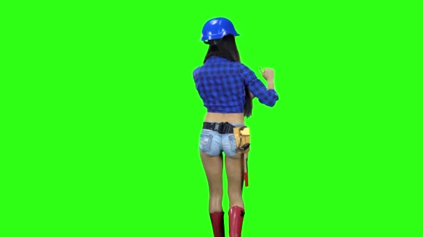 ヘルメットと緑の背景の手ジェスチャーとゆっくり歩いてショート パンツを着ている少女の背面図 — ストック動画