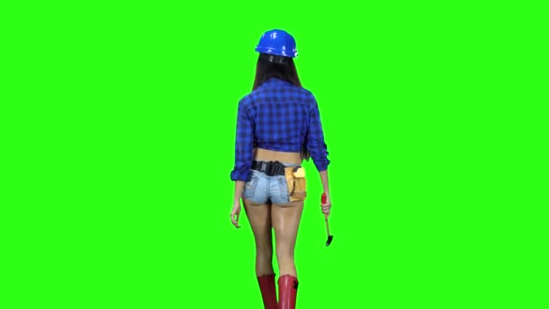 Rear view of girl in hat and shorts with a hammer in his hand walking on green background — Stock Video