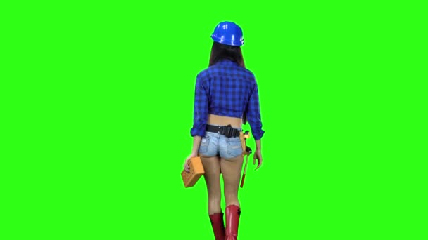 Bakifrån av flicka i hjälm och shorts med tegel i hand gå på grön bakgrund — Stockvideo