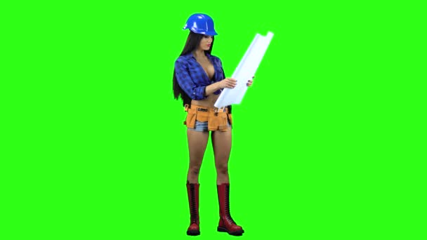 Chica en un casco y pantalones cortos desenvuelve el papel con un dibujo sobre un fondo verde — Vídeo de stock