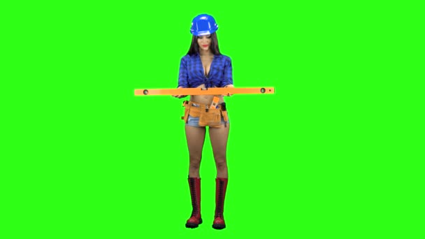 Front view of girl in helmet and shorts with level in hand standing on green background — Stock Video