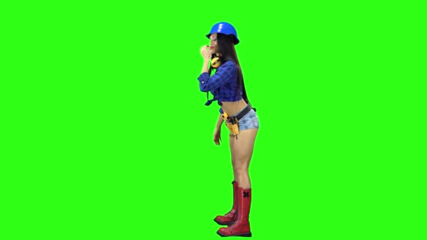 Vista lateral de la chica con casco y pantalones cortos bailando eróticamente sobre fondo verde — Vídeo de stock