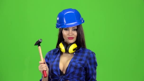 Meisje met lang haar in een helm holding hamer en kloppen ze aan de kant op groene achtergrond — Stockvideo