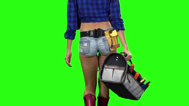 Vista trasera de chica en sombrero y pantalones cortos con una caja de herramientas en la mano caminando sobre fondo verde. En cámara lenta. De cerca. — Vídeo de stock