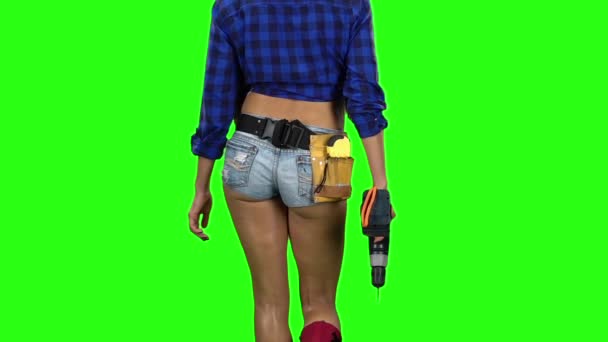 Rear view of girl in shorts with drill in hand walking on green background. Slow motion. Close up — Stock Video