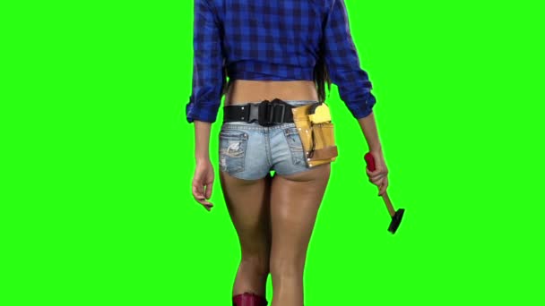 Bakifrån av tjej i shorts med en hammare i handen gå på grön bakgrund. Slow motion. Närbild — Stockvideo