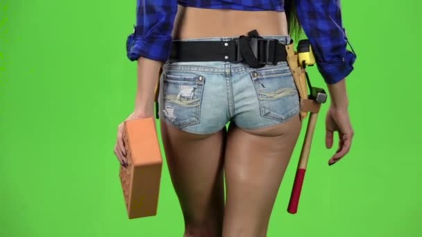 Rear view of girl in shorts with brick in hand walking on a green background. Slow motion. Close up — Stock Video
