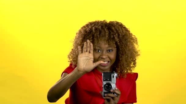 Afro amerykański fotograf posiada kamerę w jej ręce i pokazuje kciuk w. Żółte tło. Zwolnionym tempie — Wideo stockowe