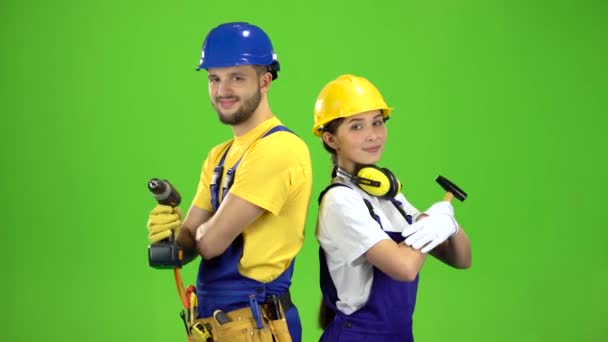 Constructor de pie un tipo sosteniendo un taladro, una chica martillo. Pantalla verde — Vídeos de Stock
