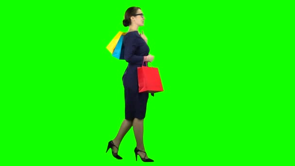 女孩与包裹购物在她的手正在沿着街道走。绿色屏幕。侧面视图 — 图库视频影像