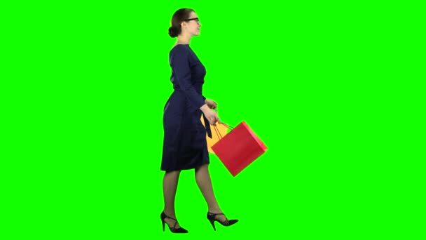 Mulher com pacotes de compras em suas mãos está andando ao longo da rua. Tela verde. Vista lateral — Vídeo de Stock