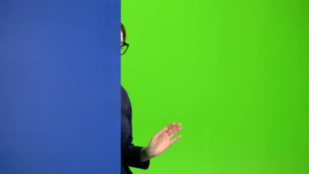Girl peeks out from behind a blue board and shows a thumbs down. Green screen — Stock Video