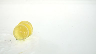 Üç ince dilim limon, su üzerinde rulo. Beyaz arka plan. Ağır çekim