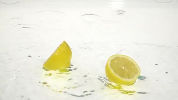 Deux moitiés de citron tombent dans l'eau. Fond blanc. Mouvement lent — Video