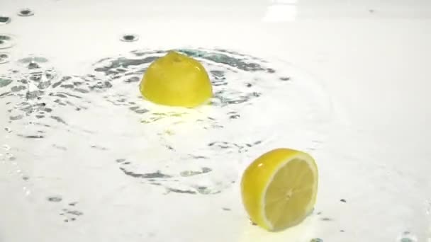 Две половинки лимона падают в воду. Белый фон. Медленное движение — стоковое видео