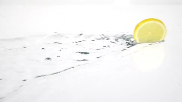 La fetta di limone sta rotolando sull'acqua. Sfondo bianco. Rallentatore — Video Stock