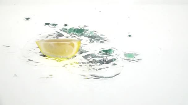 レモンの四分の一は水に落ちるし、そこに残ります。白い背景。スローモーション — ストック動画