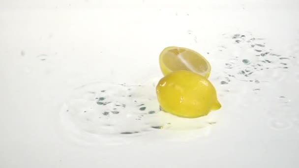 Жовтий лимон падає у воду і літає на дві частини. Білий фон. Повільний рух — стокове відео