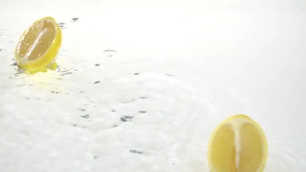 Két szelet citrom csepp a vízbe. Fehér háttér. Lassú mozgás — Stock videók