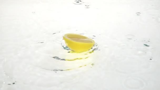 Un demi citron tombe dans l'eau. Fond blanc. Mouvement lent — Video