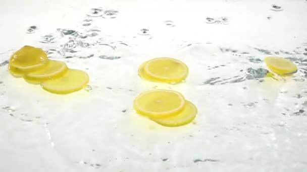 Zitrone fällt ins Wasser und Flocken auf die Lobuli. weißer Hintergrund. Zeitlupe — Stockvideo