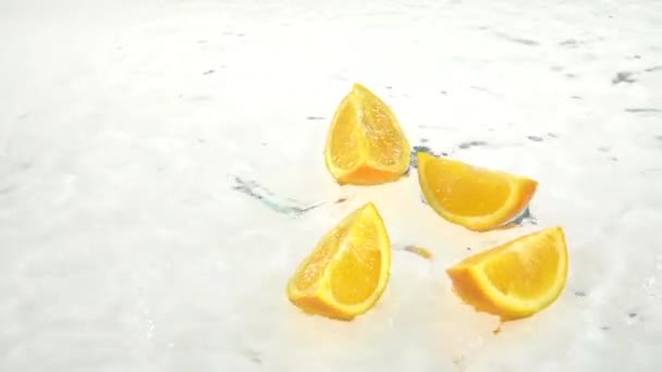 Quatro fatias de laranja caem na água. Fundo branco. Movimento lento — Vídeo de Stock