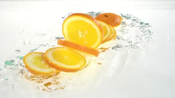Arancione cade in acqua e scaglie ai lobuli. Sfondo bianco. Rallentatore — Video Stock