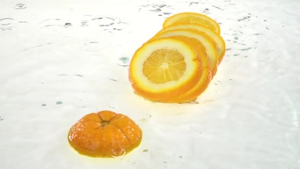 Orange fällt ins Wasser und Flocken auf die Lobuli. weißer Hintergrund. Zeitlupe — Stockvideo