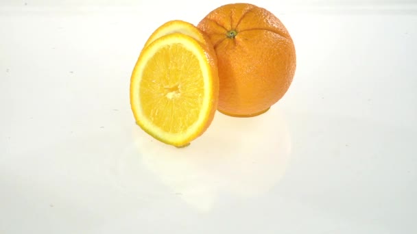 Una rebanada de naranja cae al agua. Fondo blanco. Movimiento lento — Vídeos de Stock