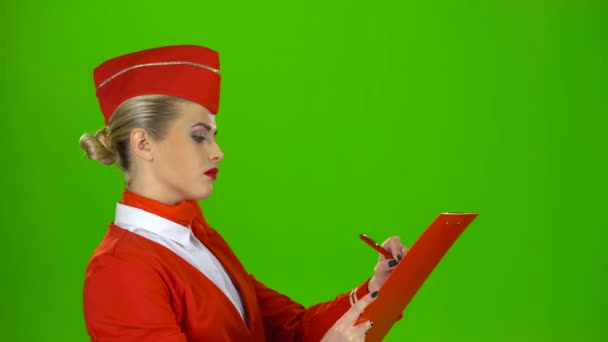 Meisje schrijft een pen in een speciale map, dat ze is een stewardess. Groen scherm. Zijaanzicht — Stockvideo