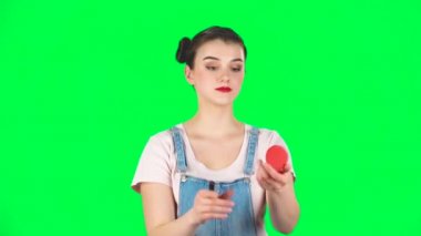 İki saçlı kadın dudaklarını boyar yeşil ekrandaki kırmızı aynaya bakar, ağır çekimde.