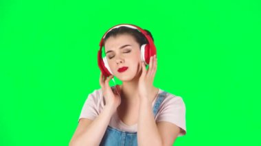 Stüdyoda yeşil ekranda büyük kırmızı kulaklıklarla dans eden kız, ağır çekim.