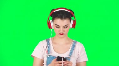 Büyük kırmızı kulaklıklı kız yeşil ekranda, ağır çekimde, cep telefonundan müzik seçiyor.