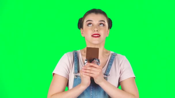 Дівчина з великим задоволенням їсть шоколад на зеленому екрані в студії, повільний рух — стокове відео