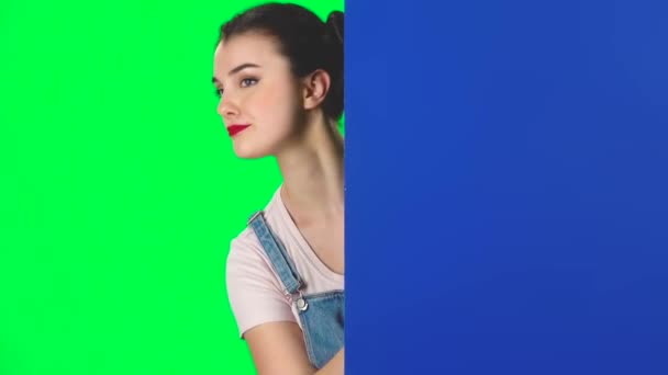 Vrouw kijkt uit van achter blauw blanco bordje en roept naar zichzelf wijzend finge, slow motion. — Stockvideo