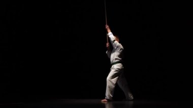 Beyaz kimonolu Kendo dövüşçüsü siyah arka planda bambu bokken ile dövüş sanatları yapıyor..