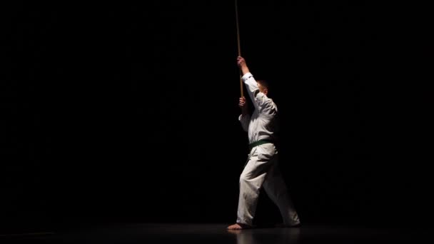 Kendo fighter on white kimono practicing martial art with the bamboo bokken on black background. — Stock Video
