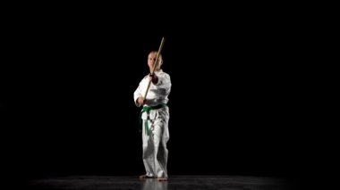 Beyaz kimonolu Kendo dövüşçüsü siyah arka planda bambu bokken ile dövüş sanatları yapıyor..
