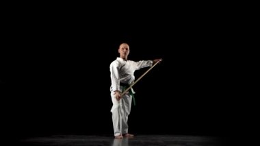Beyaz kimonolu Kendo dövüşçüsü siyah arka planda bambu bokken ile dövüş sanatları yapıyor..
