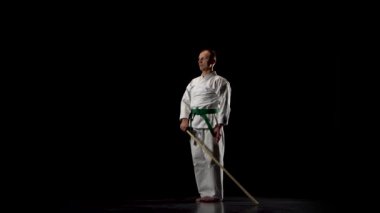 Beyaz kimonolu Kendo dövüşçüsü siyah arka planda bambu bokken ile dövüş sanatları yapıyor..