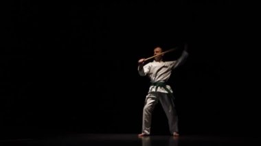 Beyaz kimonolu Kendo dövüşçüsü siyah arka planda bambu bokken ile dövüş sanatları yapıyor..