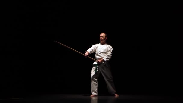 Kendo combattente su kimono bianco praticare arte marziale con il bokken di bambù su sfondo nero . — Video Stock