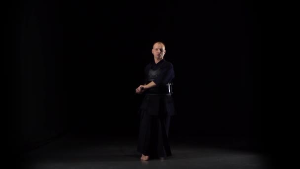 Kendo-Krieger praktiziert Kampfkunst mit dem Katana-Schwert auf schwarzem Hintergrund — Stockvideo