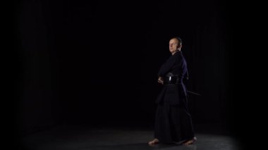Kendo savaşçısı Katana kılıcıyla siyah arka planda dövüş sanatları yapıyor.